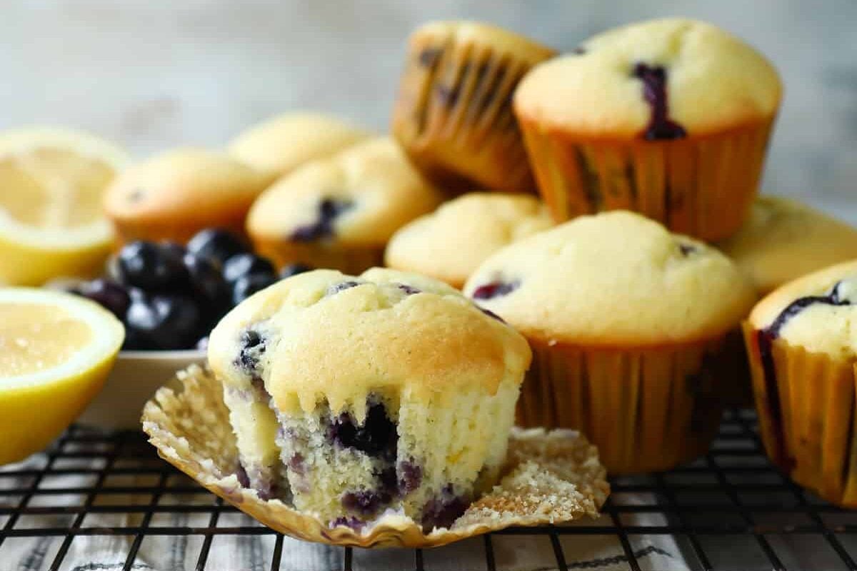 Lemon blueberry muffins on a cooling rack with a bowl of blueberries.