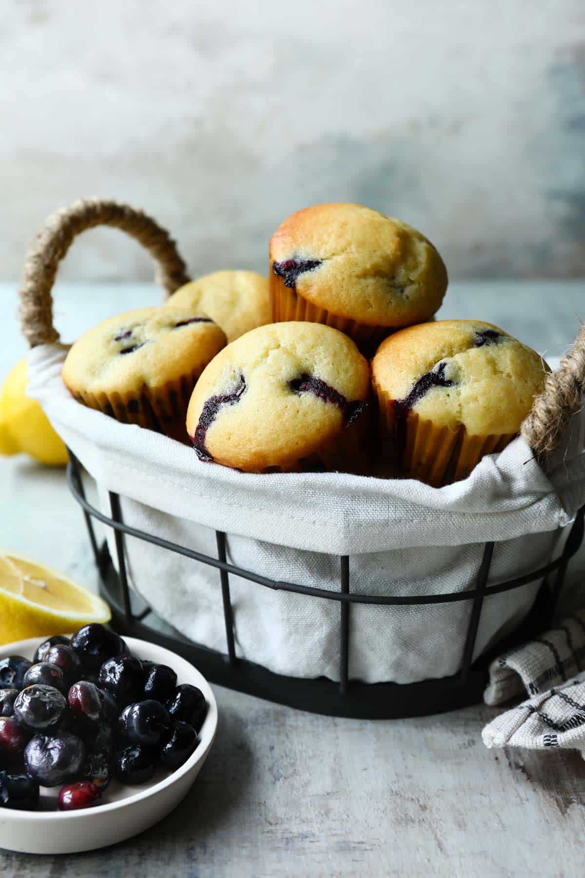 Lemon blueberry muffins in a basket with a bowl of blueberries.