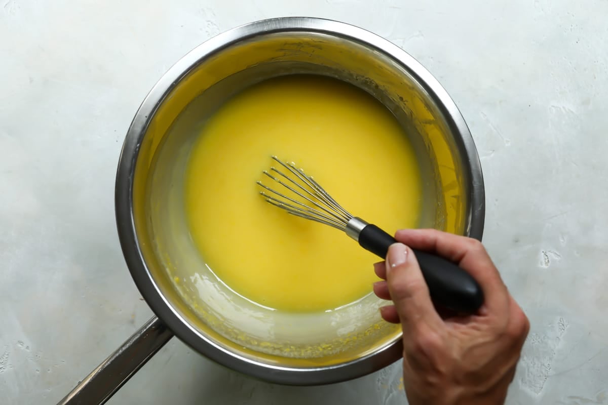 Lemon curd being whisked in a silver bowl.