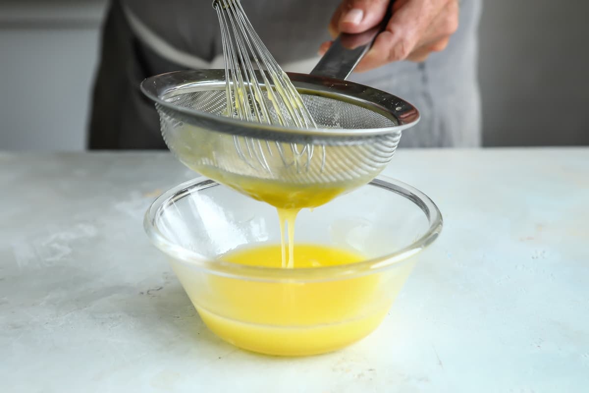 Lemon curd being strained into a small clear bowl.