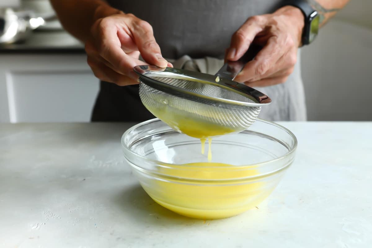 Lime curd being strained into a small clear bowl.