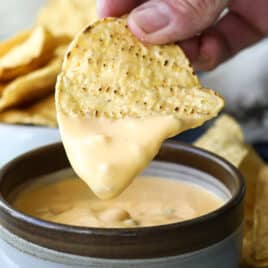 A tortilla chip being dipped in nacho cheese.