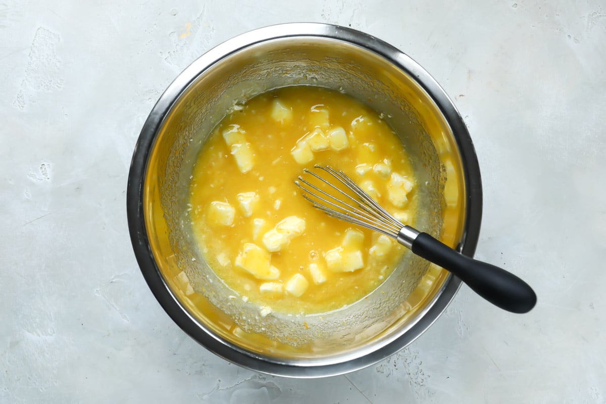 A silver mixing bowl with a whisk and the start of orange curd.