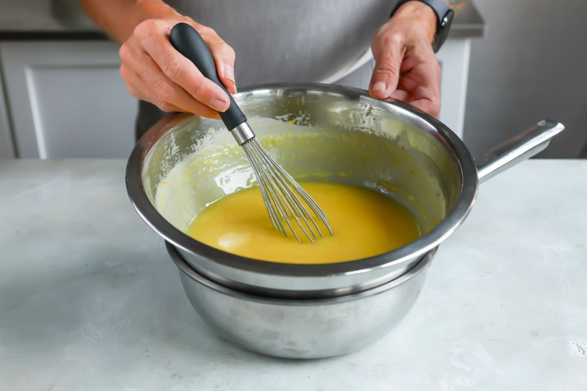 Someone stirring orange curd in a silver bowl with a whisk.