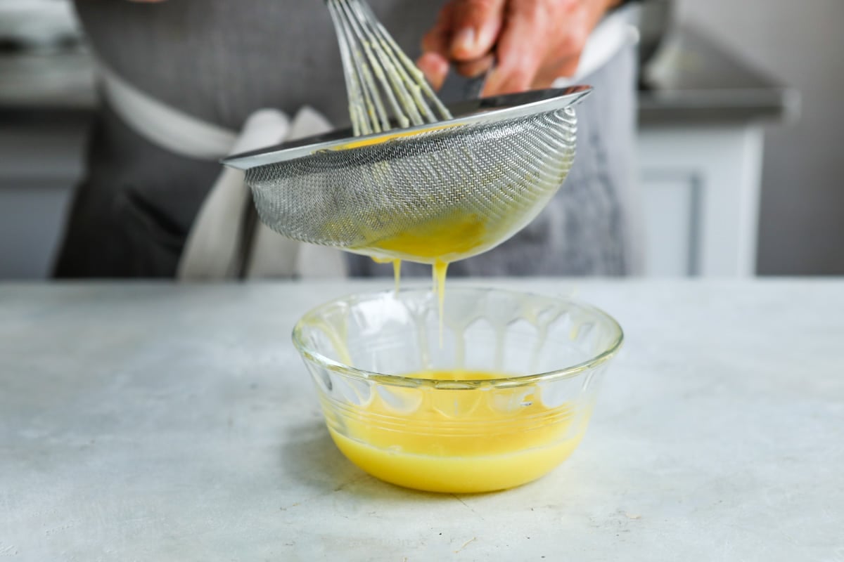 Orange curd being strained into a small clear bowl.
