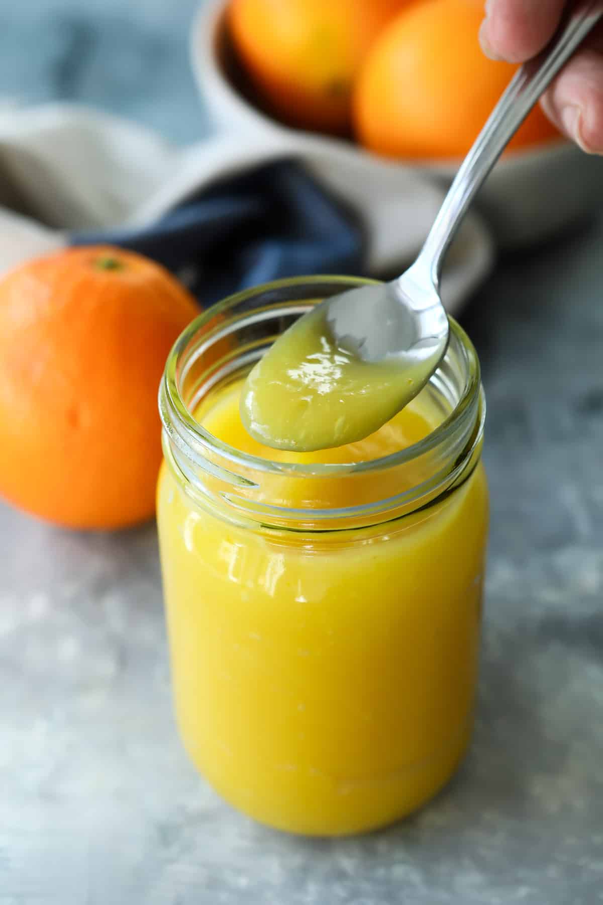 Orange curd being scooped out of a clear jar with a teaspoon.