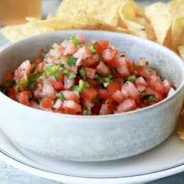 A bowl of pico de gallo on a plate with tortilla chips.