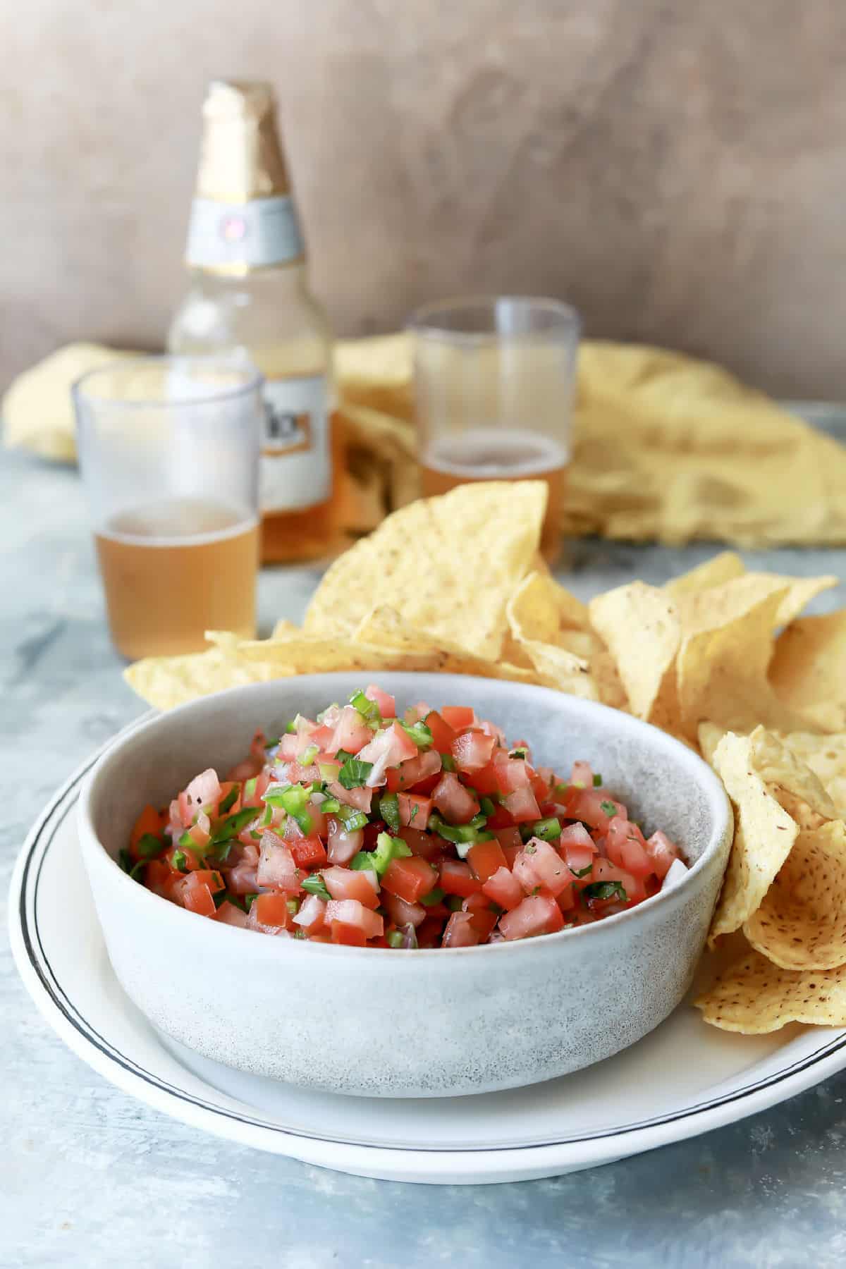 A bowl of pico de gallo on a plate with tortilla chips.