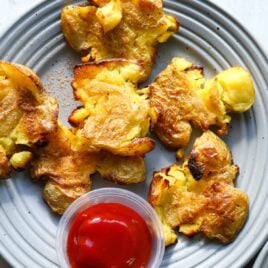 Smashed potatoes on three small gray plates.