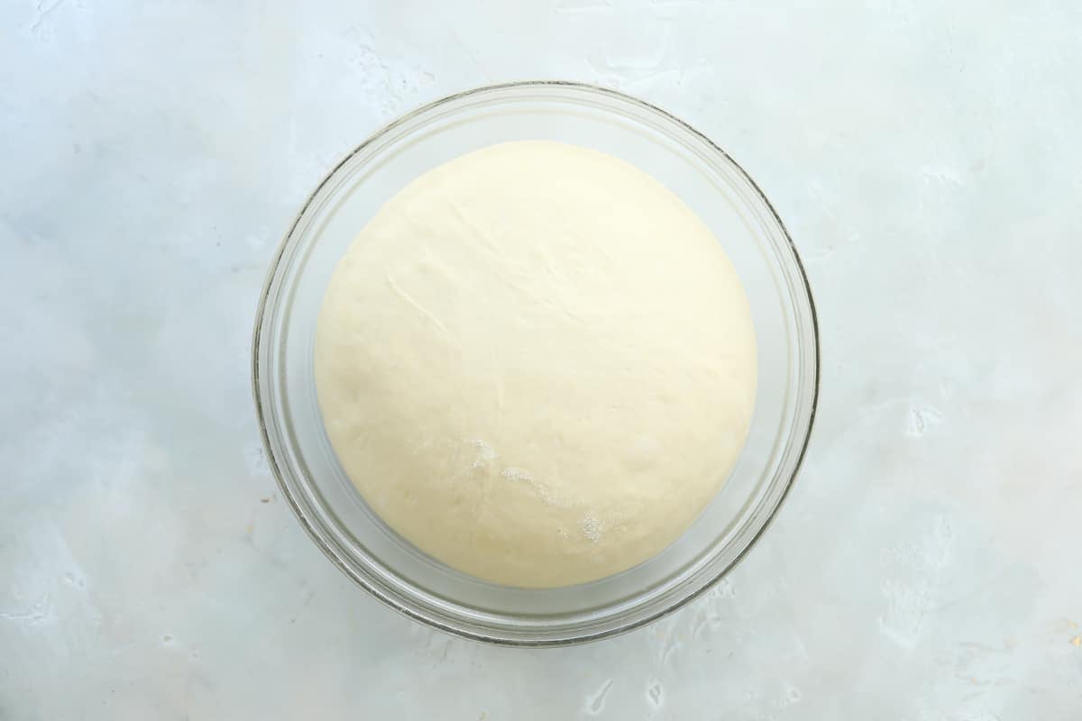 Dough for soft yeast dinner rolls in a large glass bowl after it has risen.