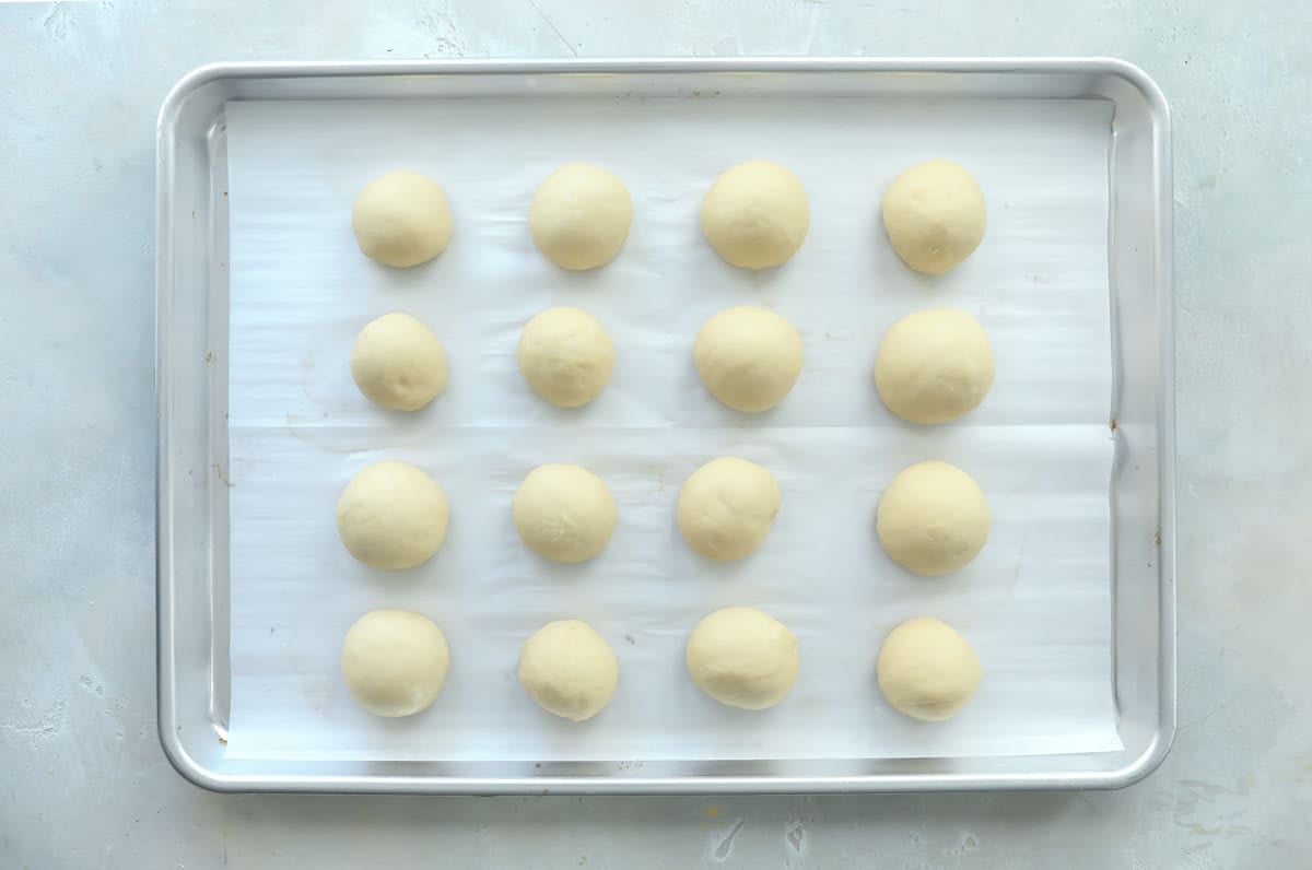 Balls of dough for soft yeast dinner rolls on a baking sheet.