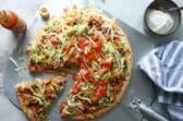 A taco pizza with a slice cut.