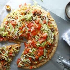 A taco pizza with a slice cut.