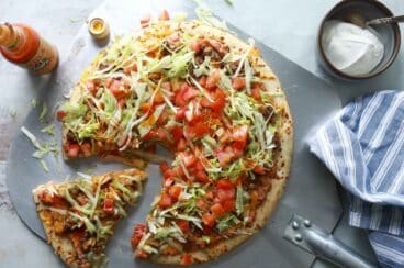 A taco pizza with a slice cut.