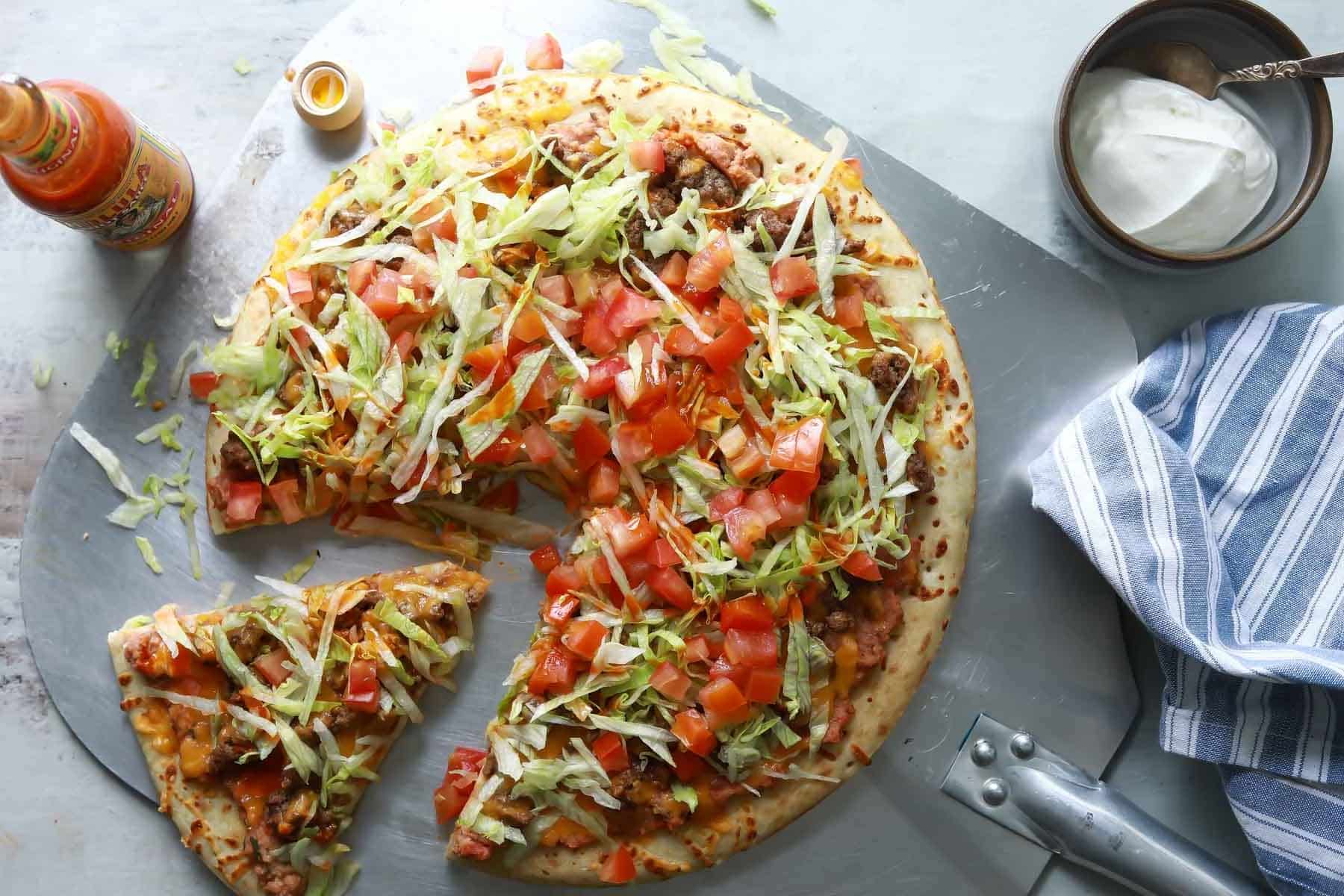 A taco pizza with a slice cut.