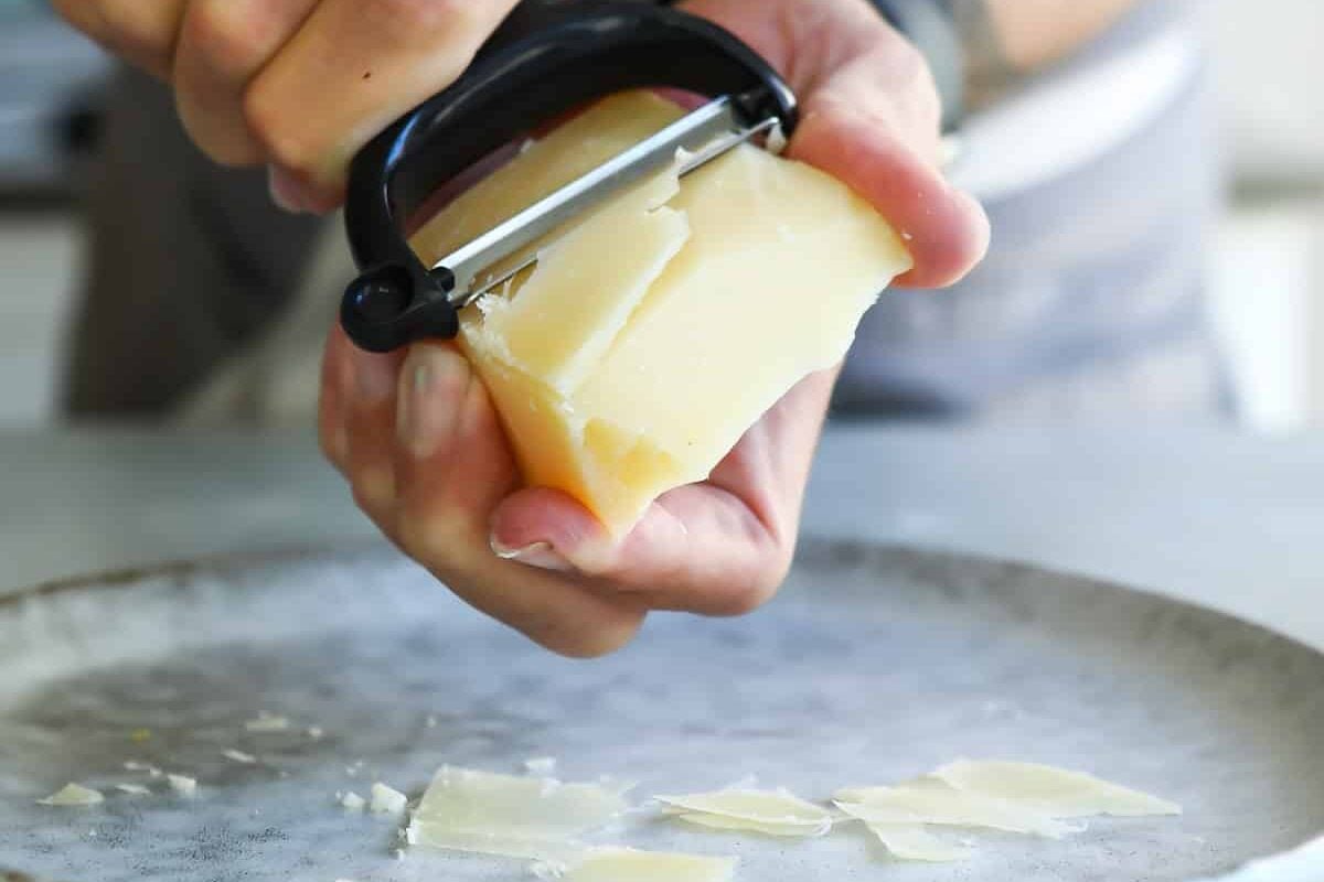 Shaving strips of parmesan cheese with a vegetable peeler.