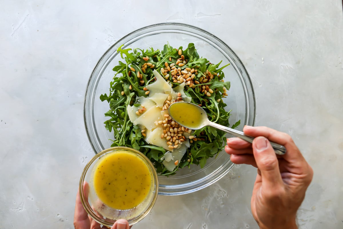 A bowl of arugula salad with pine nuts.