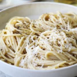 Someone taking a fork of Cacio e pepe out of a white bowl.