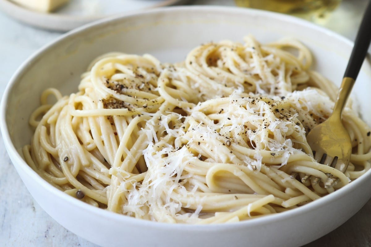Someone taking a fork of Cacio e pepe out of a white bowl.