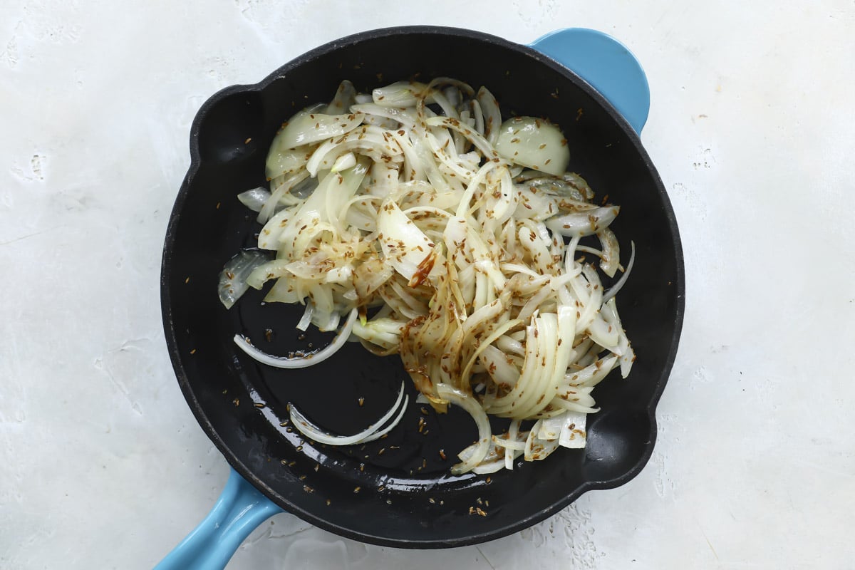 A skillet full of cooked onions and cumin seeds.