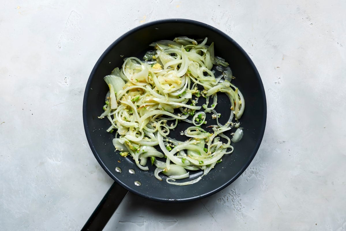 A skillet of onions cooking for eggplant curry.