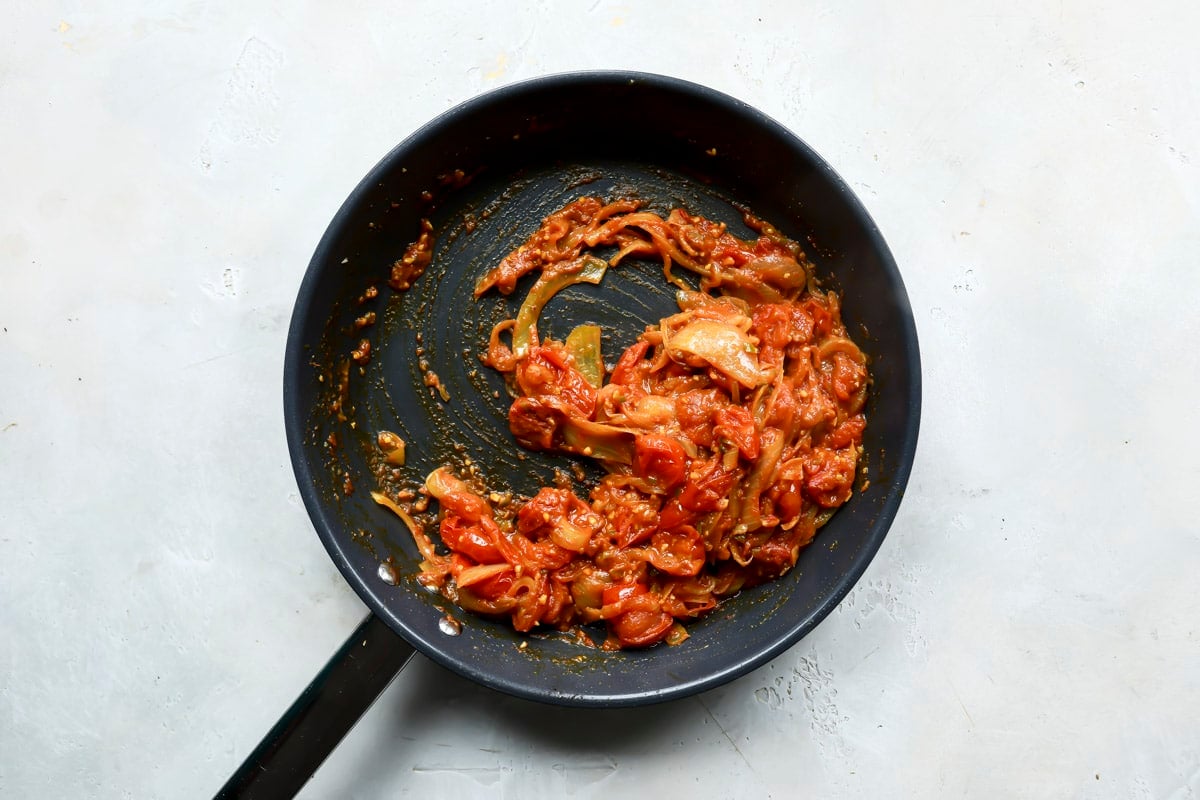 A skillet of onions and tomatoes cooking for eggplant curry.