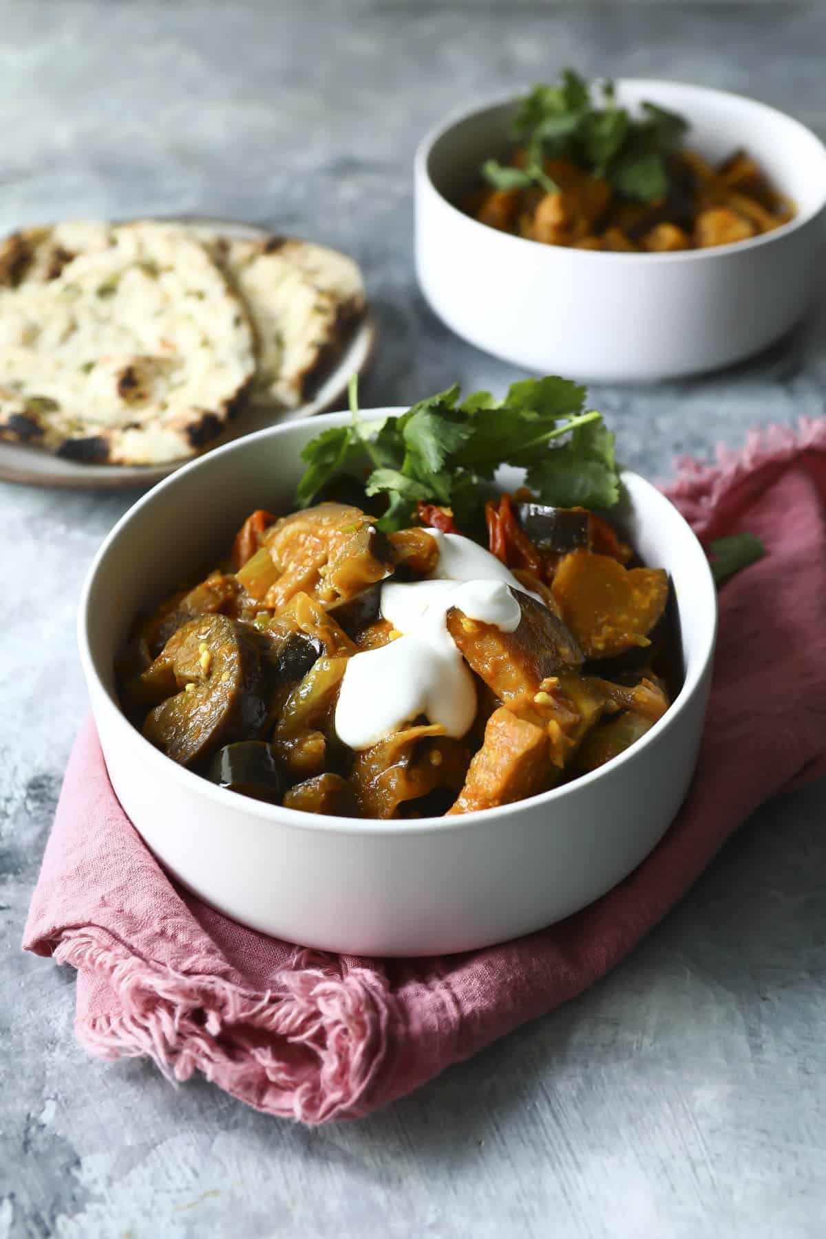 A bowl of eggplant curry with yogurt on top.