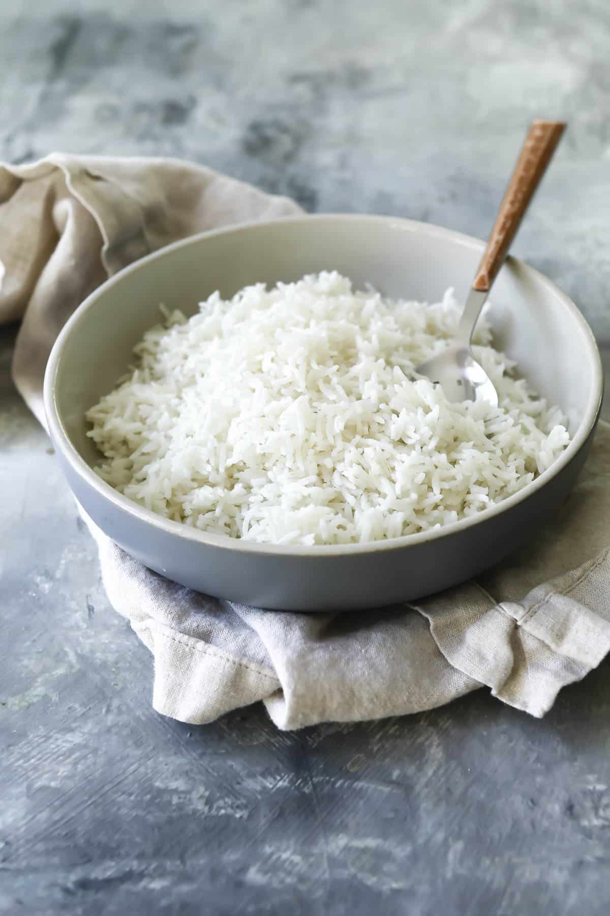 A serving bowl of basmati rice with a spoon resting in it.