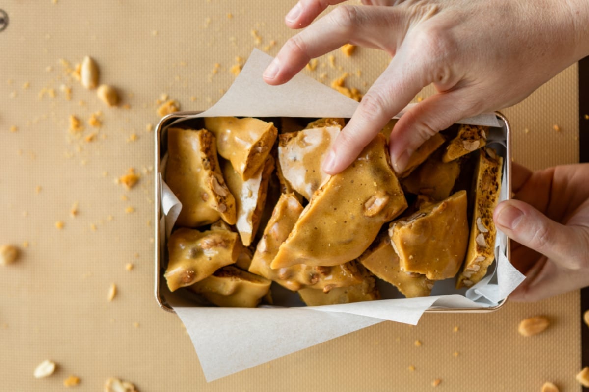 Someone holding a box of pieces of peanut brittle.