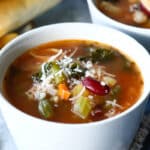 Two bowls of Olive Garden Minestrone soup next to breadsticks.