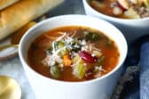 Two bowls of Olive Garden Minestrone soup next to breadsticks.