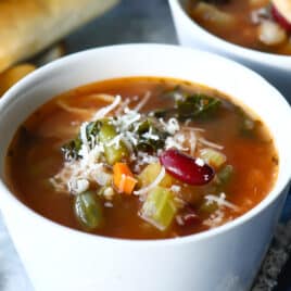 Two bowls of Olive Garden Minestrone soup next to breadsticks.