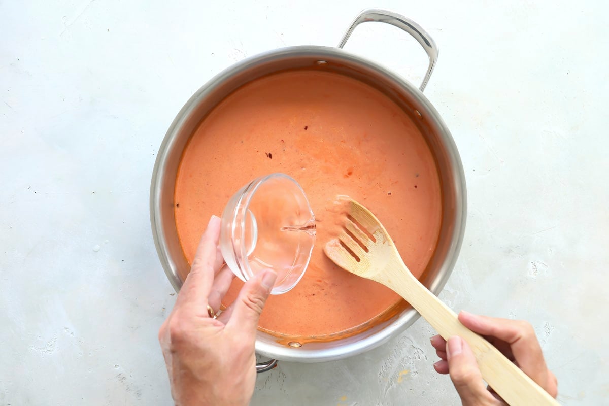 Vodka being added into tomato sauce mixture.