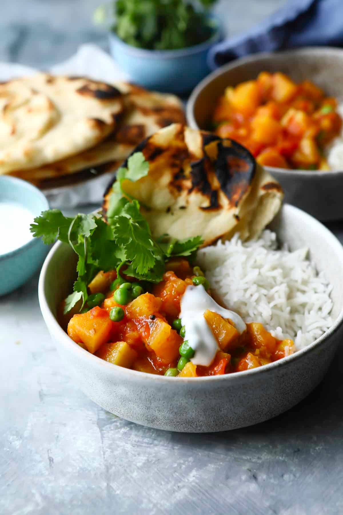 A bowl of potato curry with rice and naan on the side.