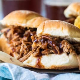 A plated with pulled pork sandwiches and chips on it.