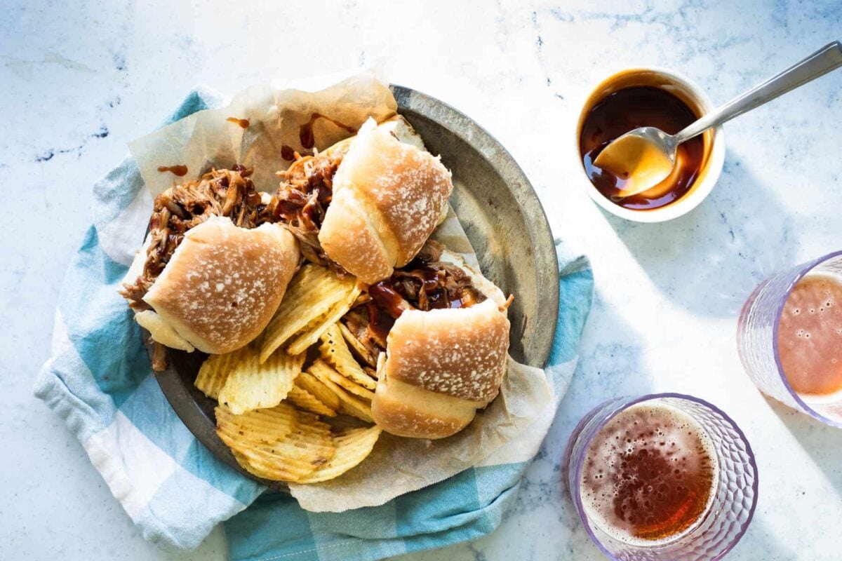A plated with pulled pork sandwiches and chips on it.