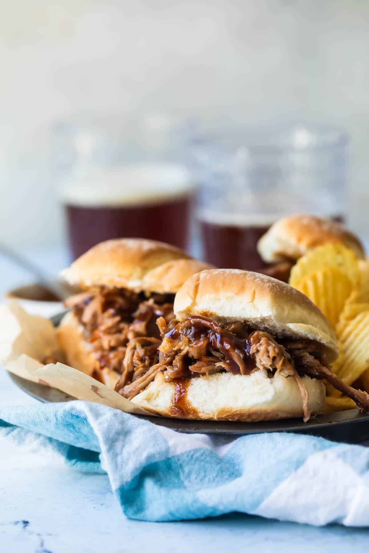 A plated with pulled pork sandwiches and chips on it.