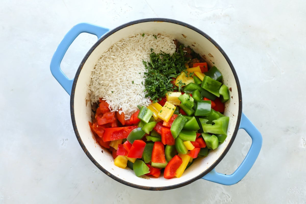 Rice, parsley and bell pepper chunks being added to the meat mixture for stuffed pepper casserole.