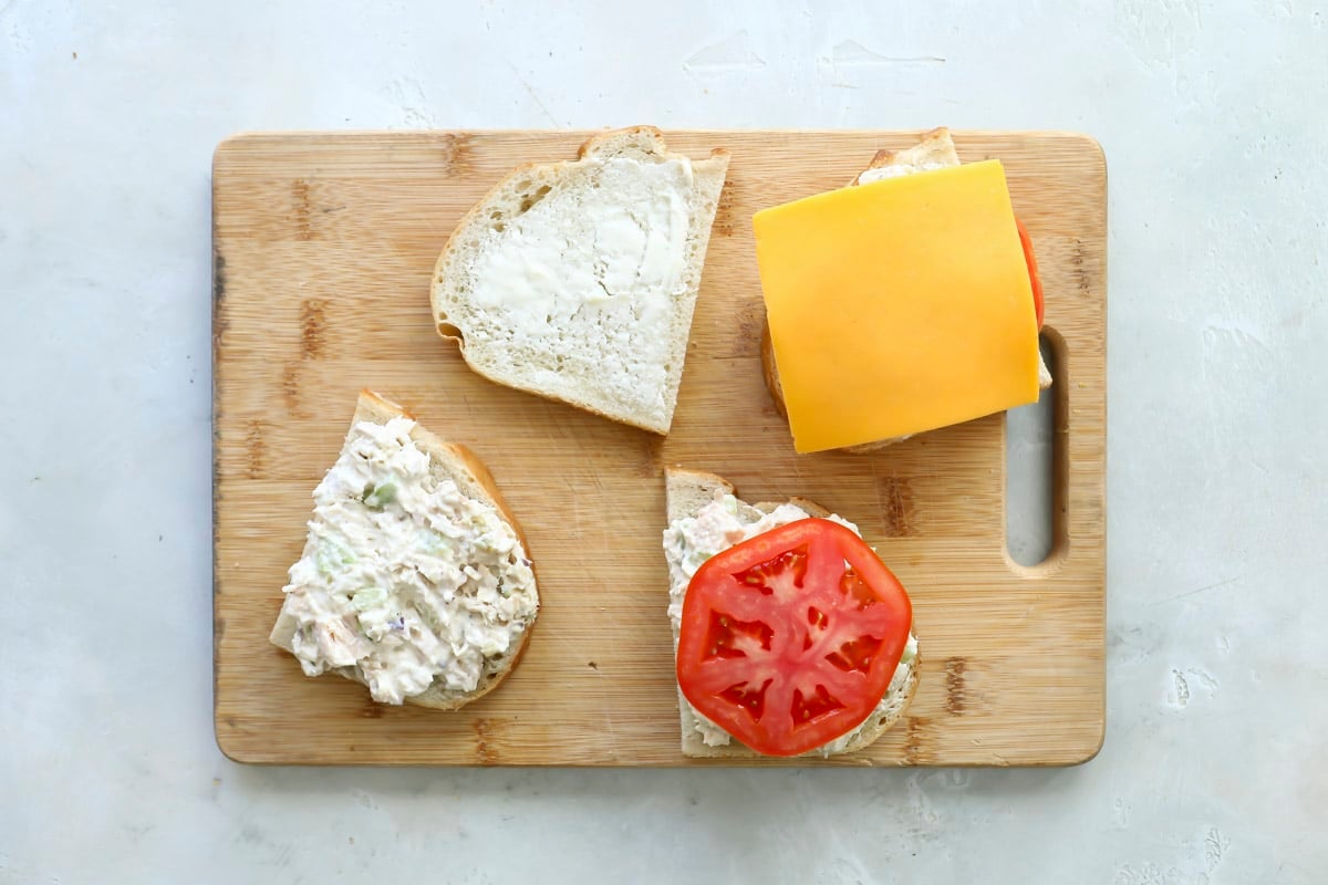 A tuna melt being assembled on a wooden cutting board.
