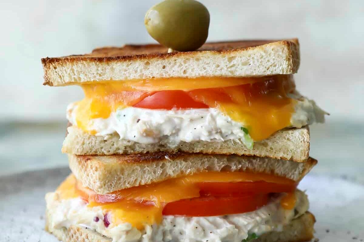 Two tuna melt halves stacked on a gray plate being held together with a toothpick with an olive on it.