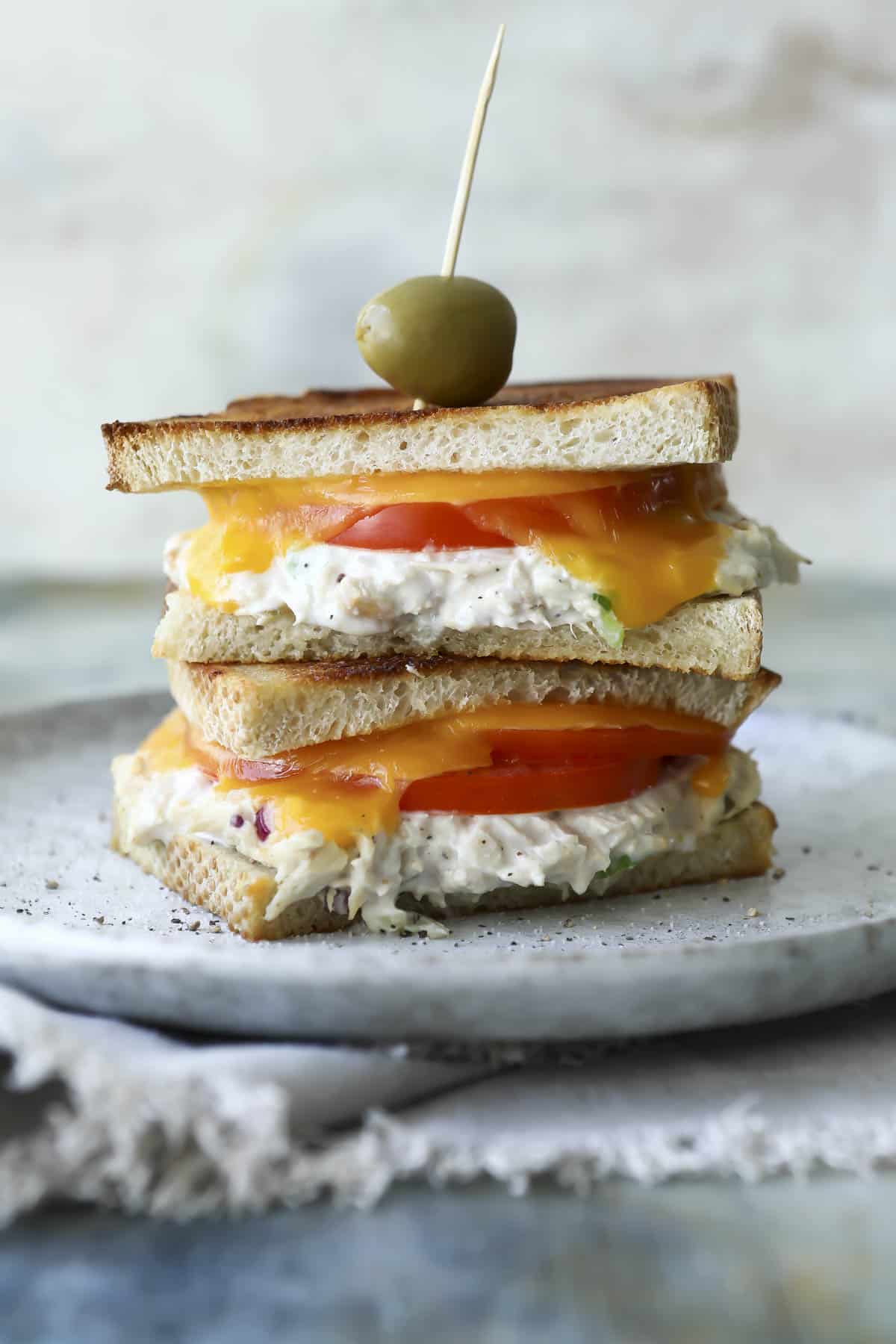 Two tuna melt halves stacked on a gray plate being held together with a toothpick with an olive on it.