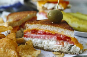 A halved tuna melt on parchment paper next to kettle chips.