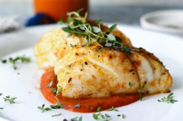 A piece of air fryer cod served over romesco sauce.