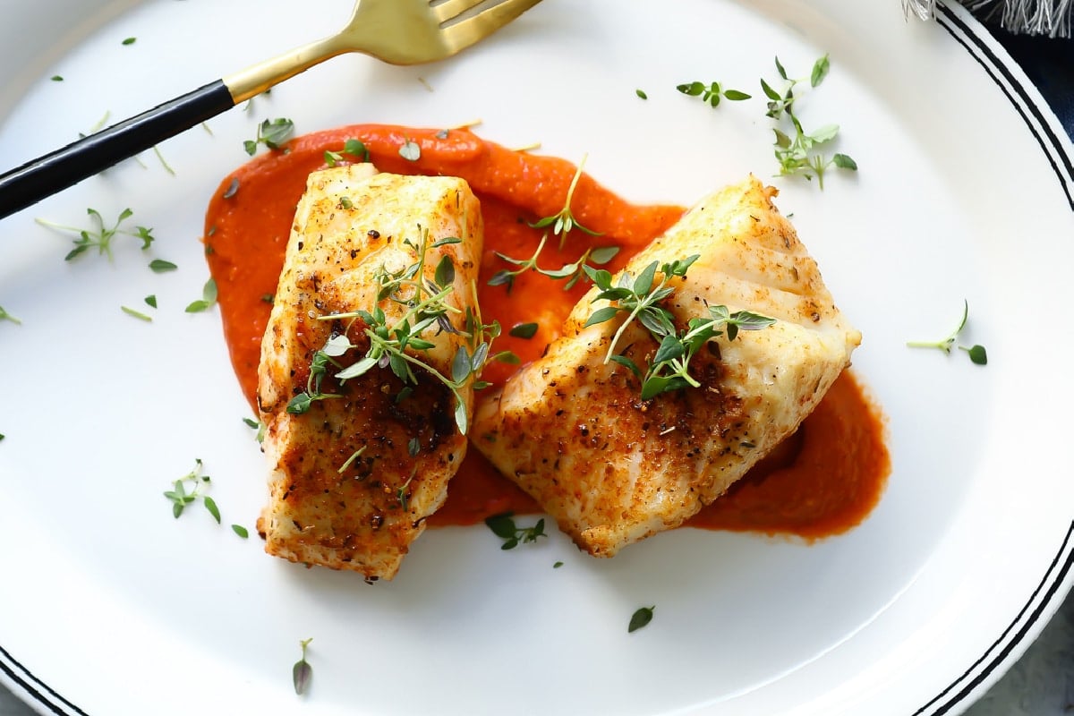 A piece of air fryer cod served over romesco sauce.