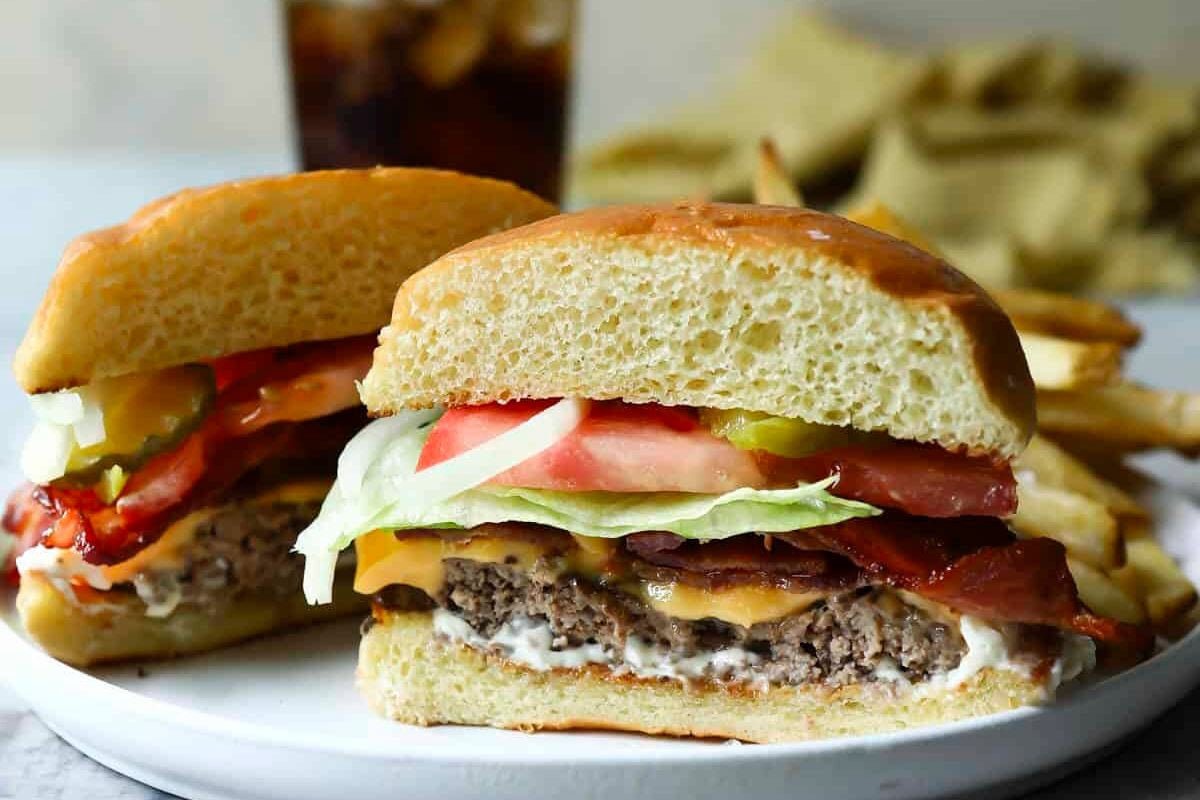 A plate with a halved bacon cheeseburger and fries.