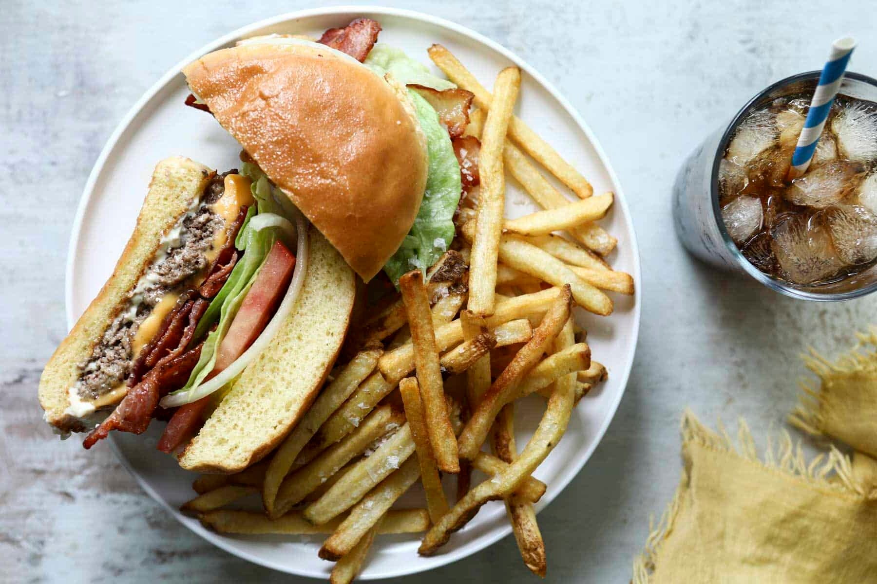 Two halves of a bacon cheeseburger on a plate with fries.