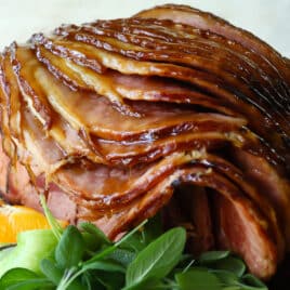 A sliced baked ham on a platter with fresh herbs and oranges.