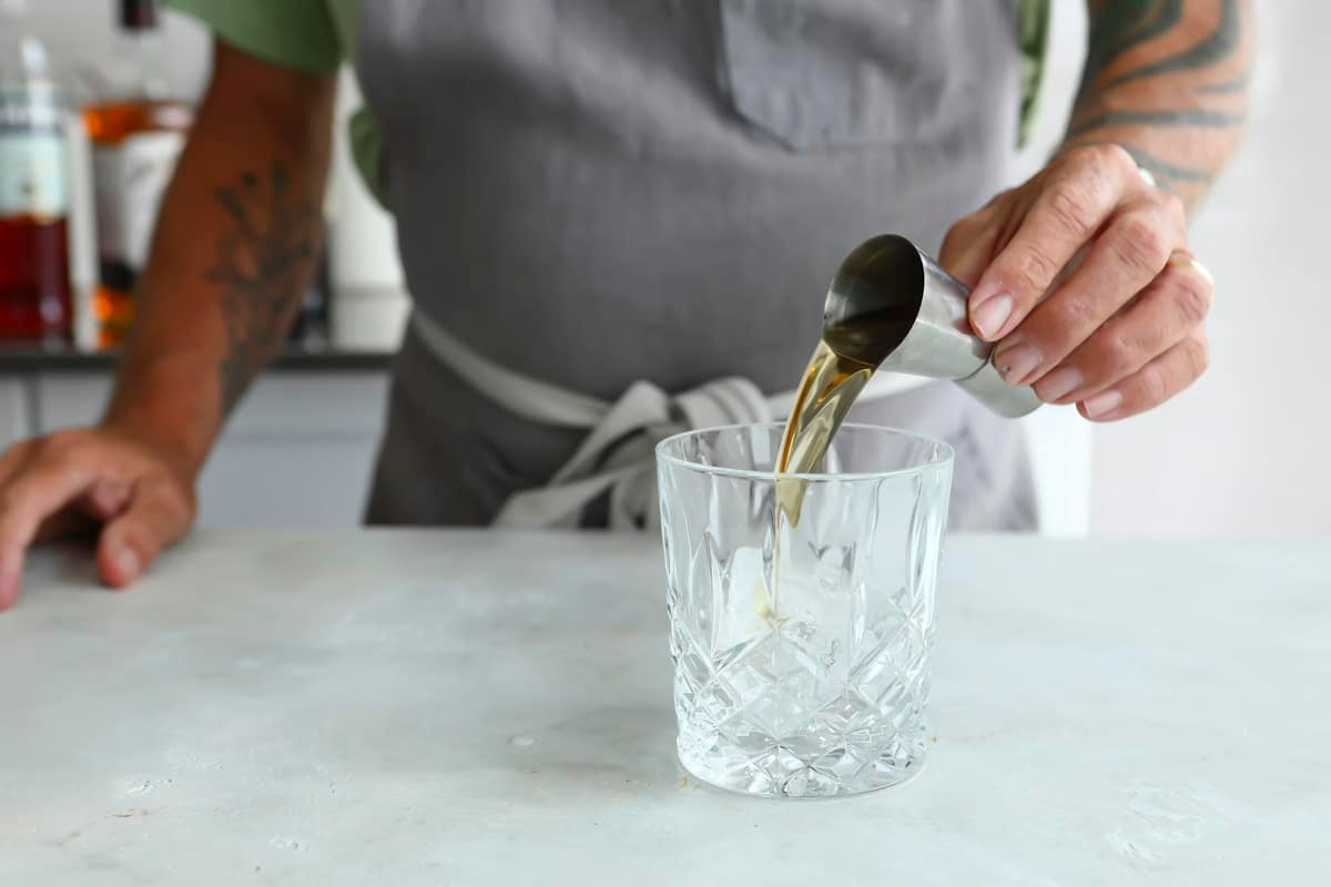 Someone pouring a shot of whiskey into an on the rocks glass.
