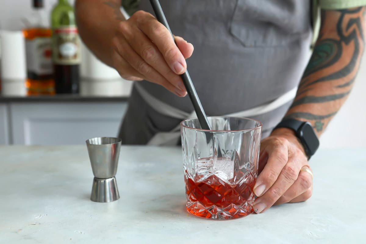 Someone mixing a boulevardier cocktail in an on the rocks glass.