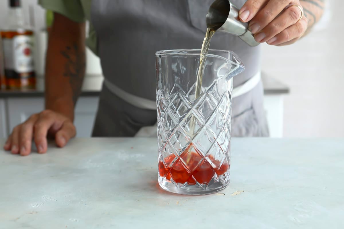 Ingredients for a boulevardier cocktail being added into a mixing cup.